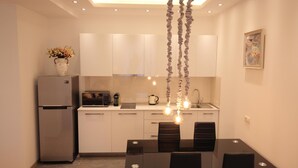 A modern kitchen with a refrigerator, microwave, and coffee maker. There is a dining table with chairs and pendant lights. - Superior Apartments (Tbilisi)