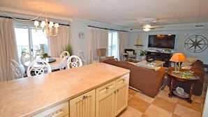A well-lit living room with a sofa, TV, and a dining area with chairs and a table. - Harbour Island 102M 2 Bedroom Condo by RedAwning (Ocean City)