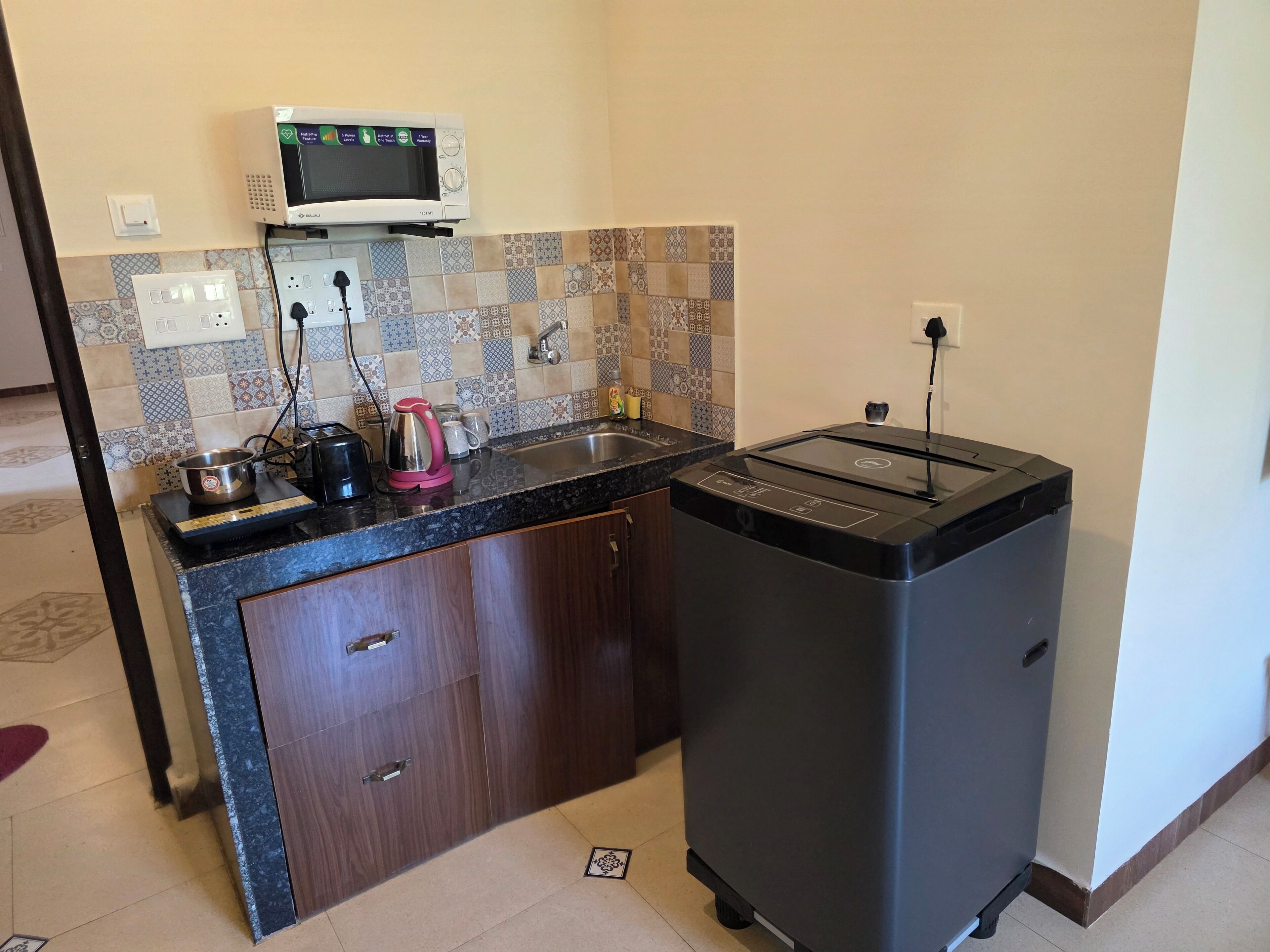 A compact kitchen with a microwave, toaster, kettle, and sink.