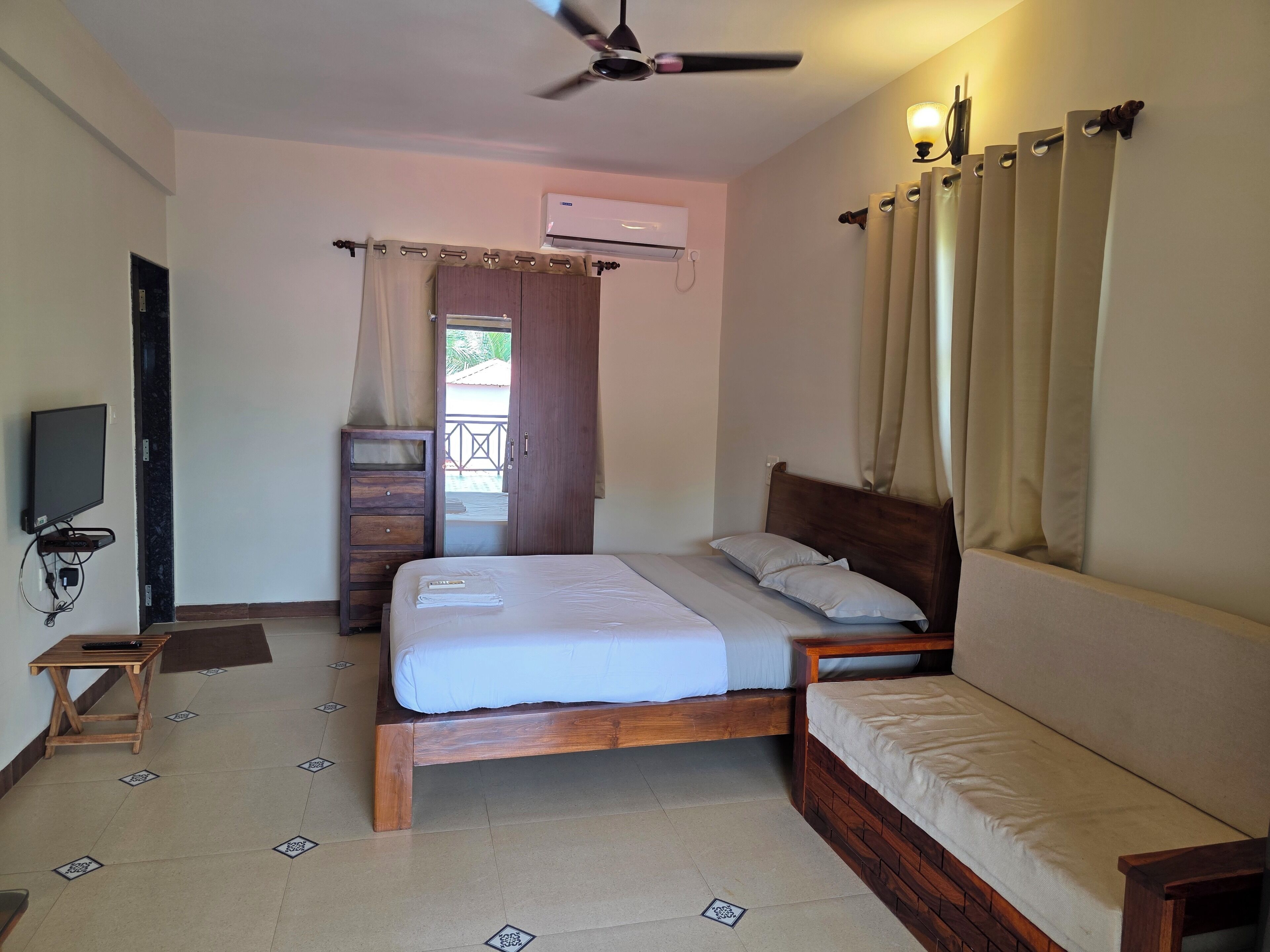 A bedroom with a bed, a TV, a ceiling fan, and a window with curtains.
