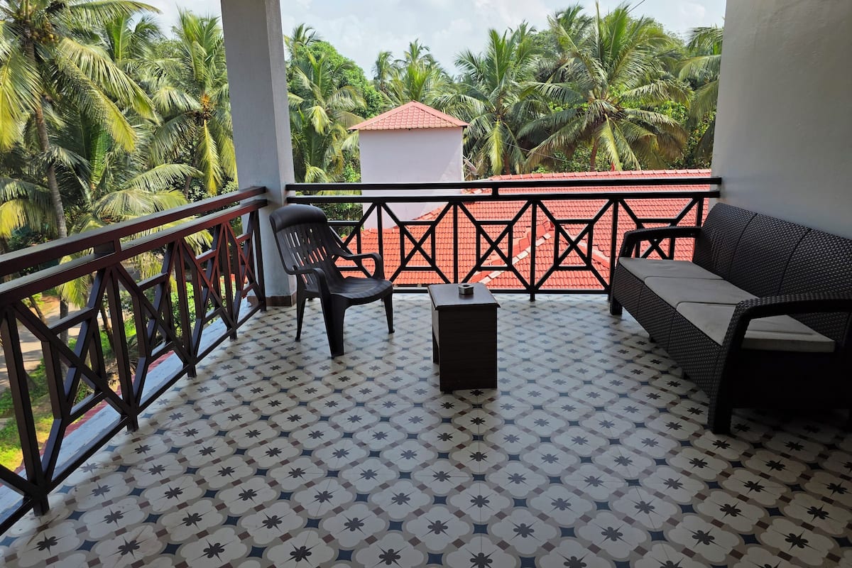 Een balkon met een vloer met patroon, een zwarte stoel, een kleine tafel en een rieten bank.