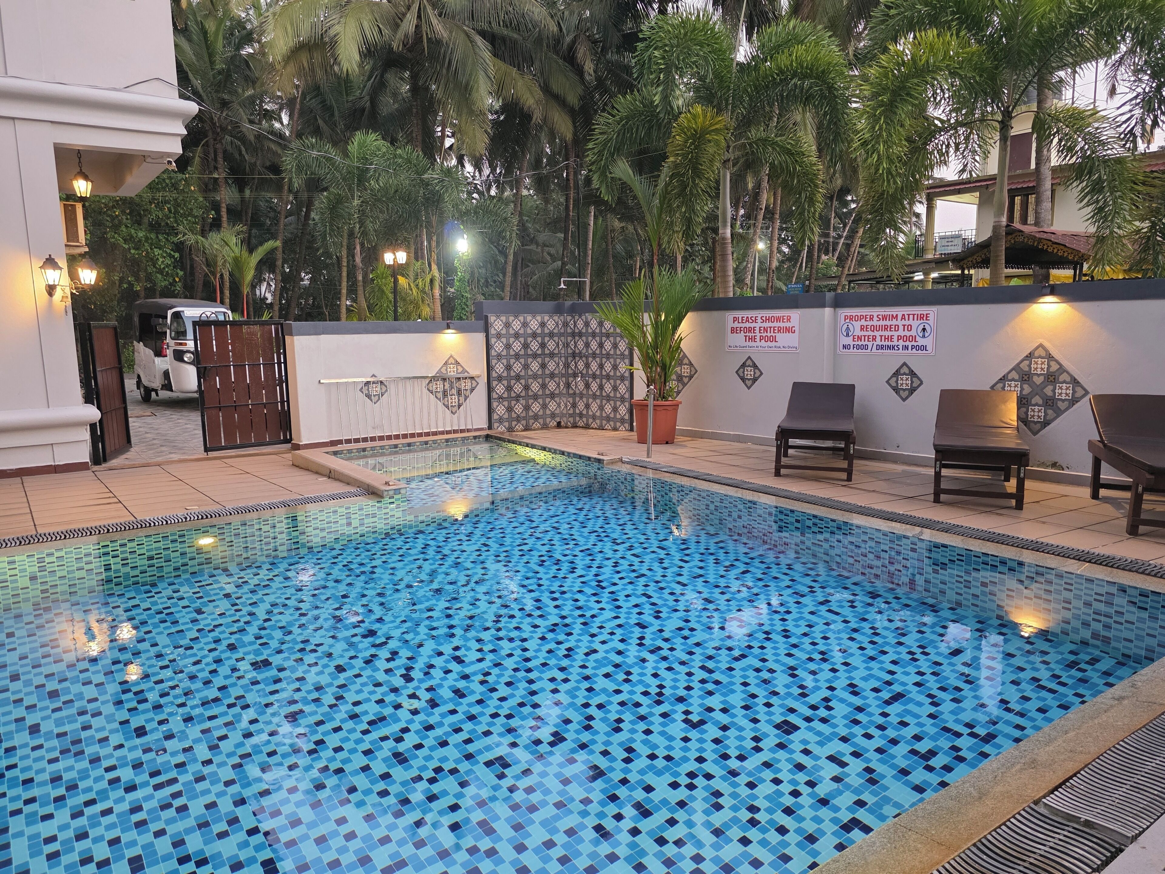 Une piscine avec un rev êtement de sol carrelé, des chaises longues et un panneau indiquant les règles concernant la douche et les vêtements appropriés pour la piscine.