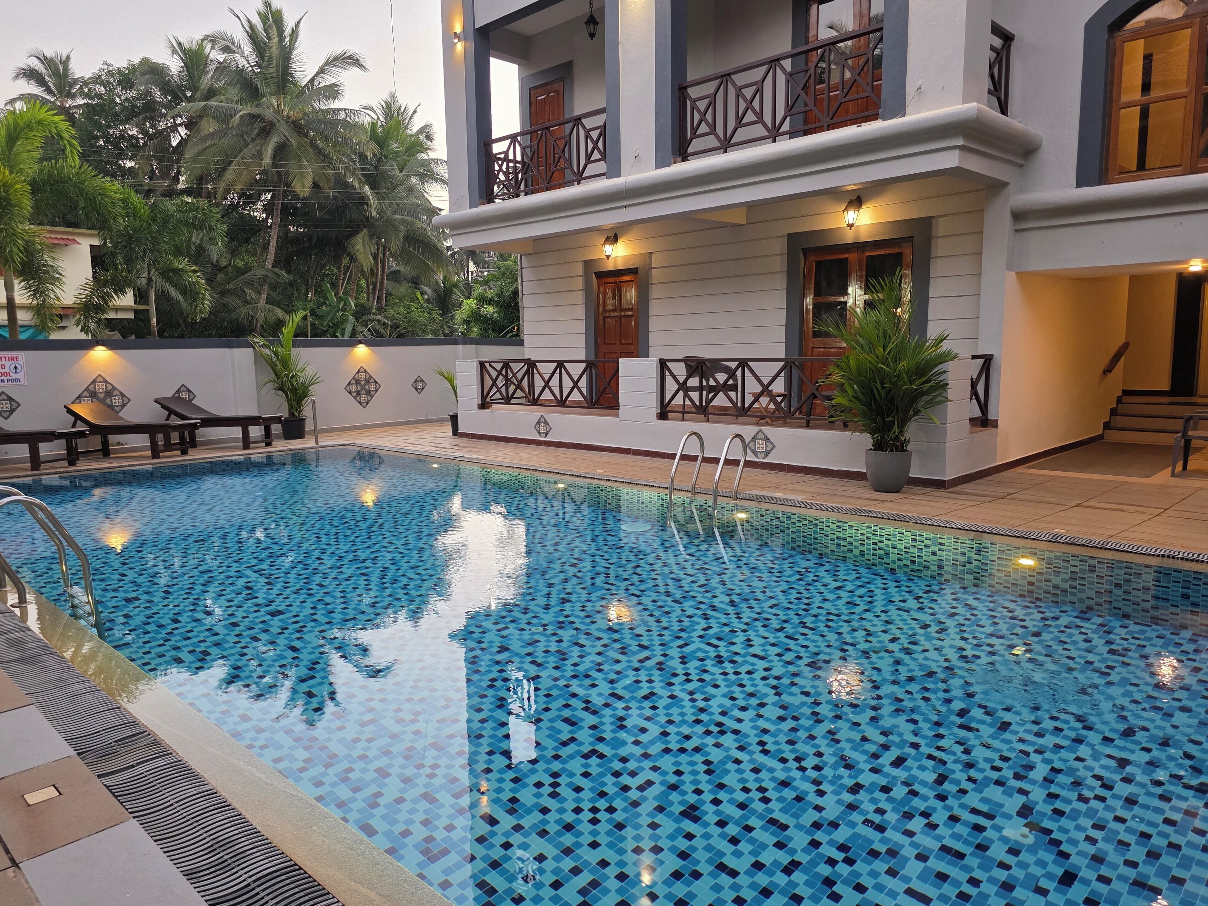 A swimming pool with a tiled pattern, surrounded by a building with balconies and a staircase.