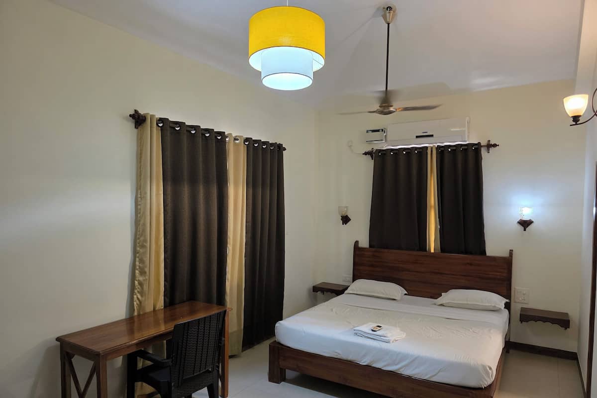 Een slaapkamer met een bed, een bureau en een stoel. Er is een plafondventilator en een airconditioning.