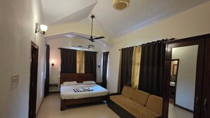 A hotel room with a bed, a sofa, a ceiling fan, and a large mirror. - Coastal Suites Apart-Hotel (Benaulim)