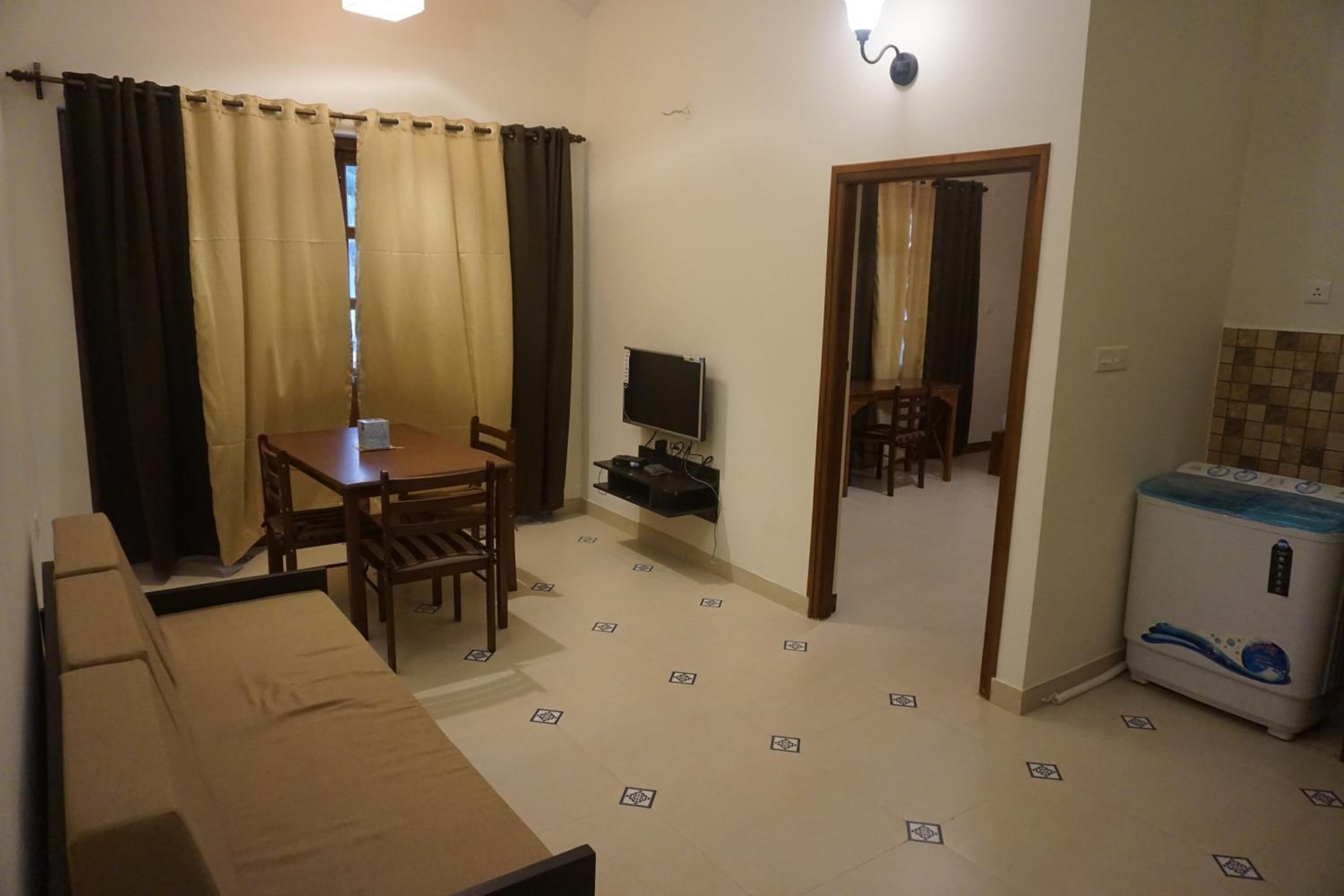 Una habitación compacta con sofá, una mesa de comedor con sillas, televisor, lavadora y una puerta que da a otra habitación.