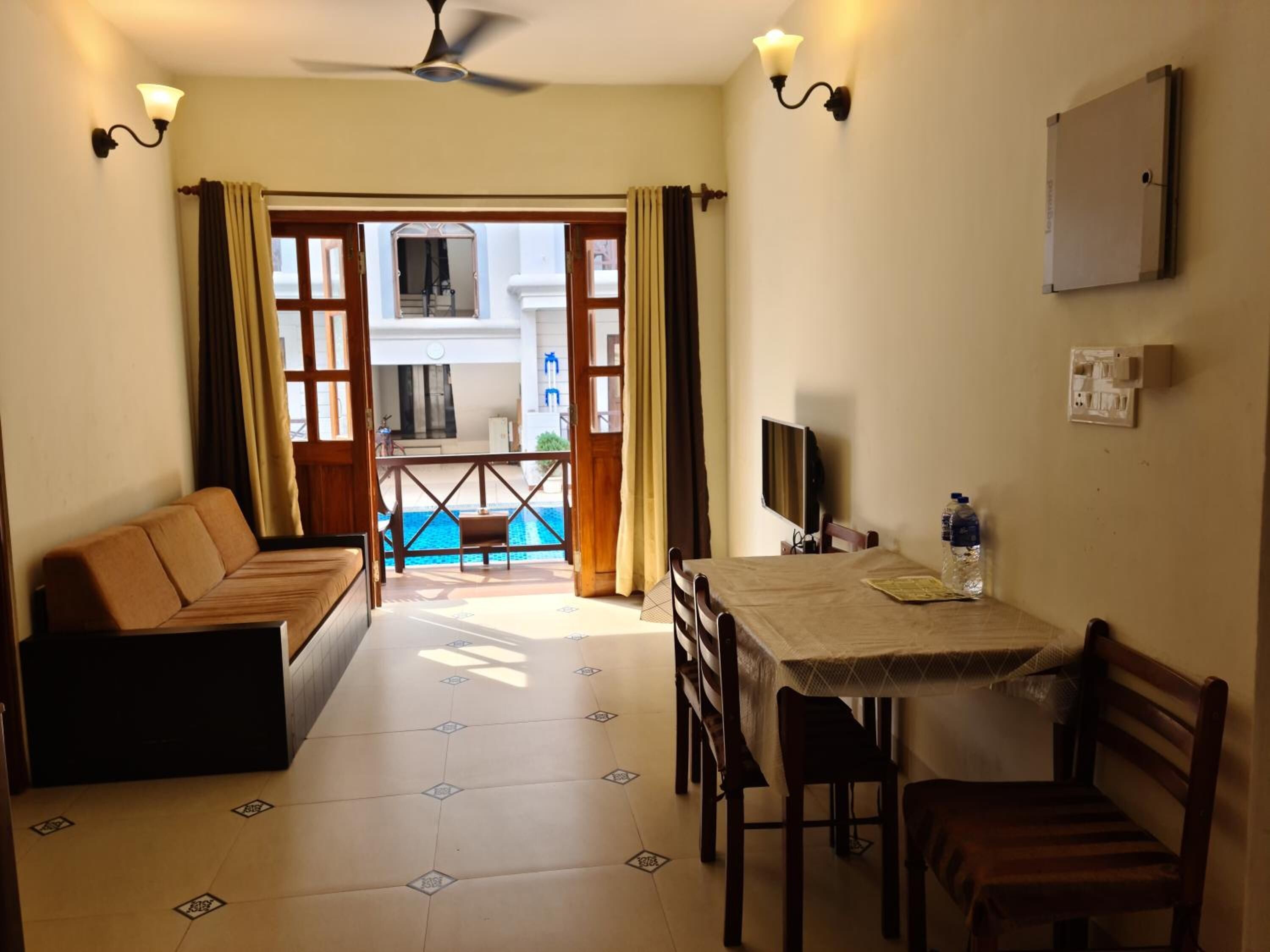 Une pièce comprenant un canapé, une table à manger avec des chaises, un téléviseur et une vue sur une piscine par une porte ouverte.
