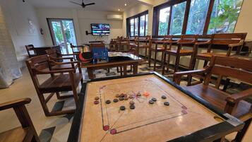 Una habitación con mesa de fútbol, sillas de madera, televisor y ventanas amplias con vista a follaje.