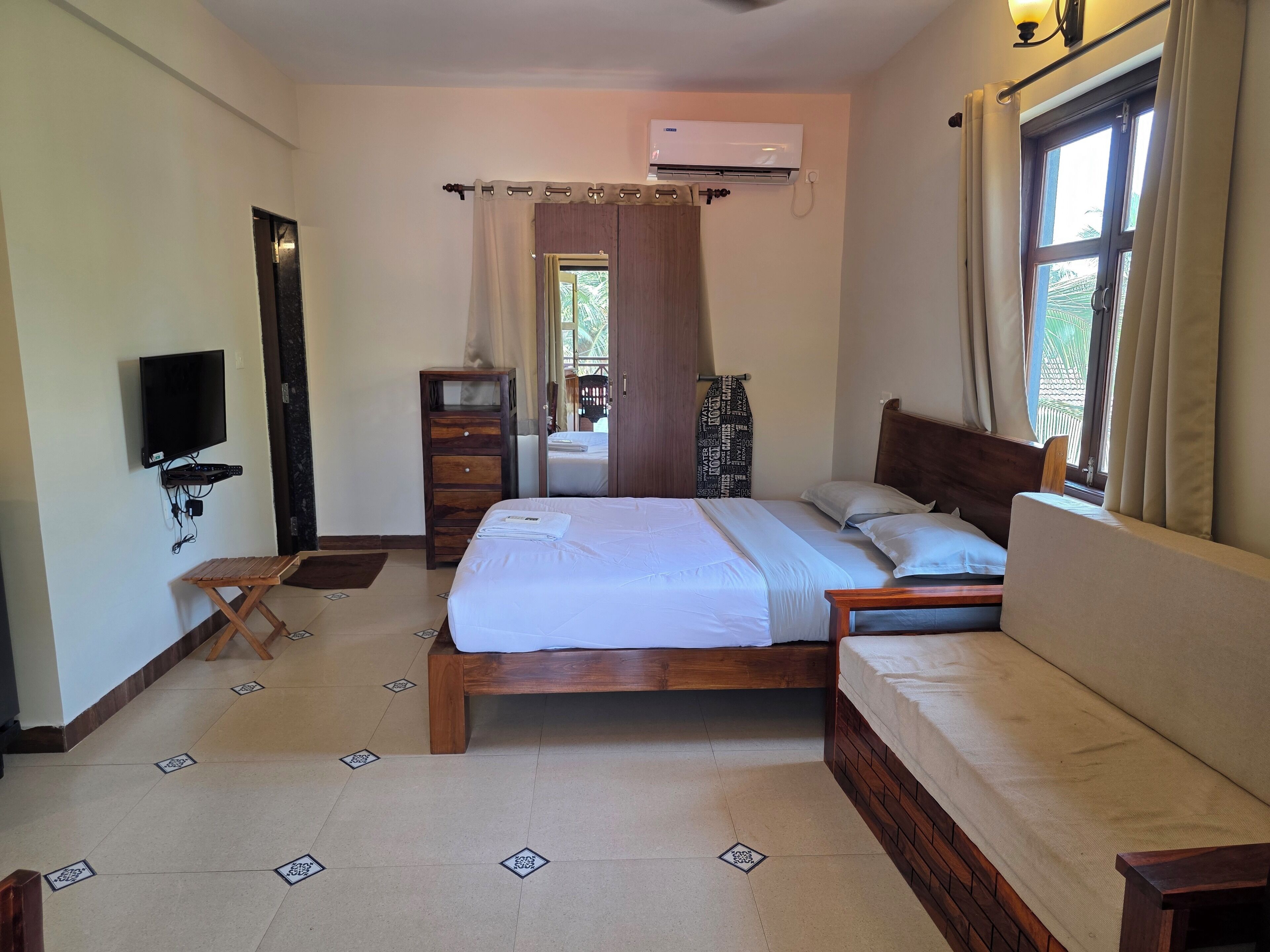 A bedroom with a bed, a TV mounted on the wall, a wooden dresser, and an air conditioning unit.