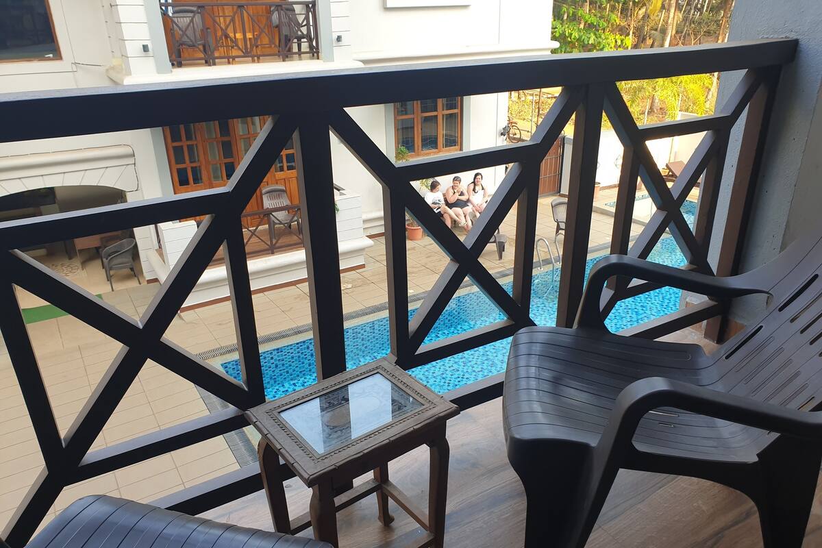 Een balkon met een zwembad, houten meubels en uitzicht op een huis met een balkon.
