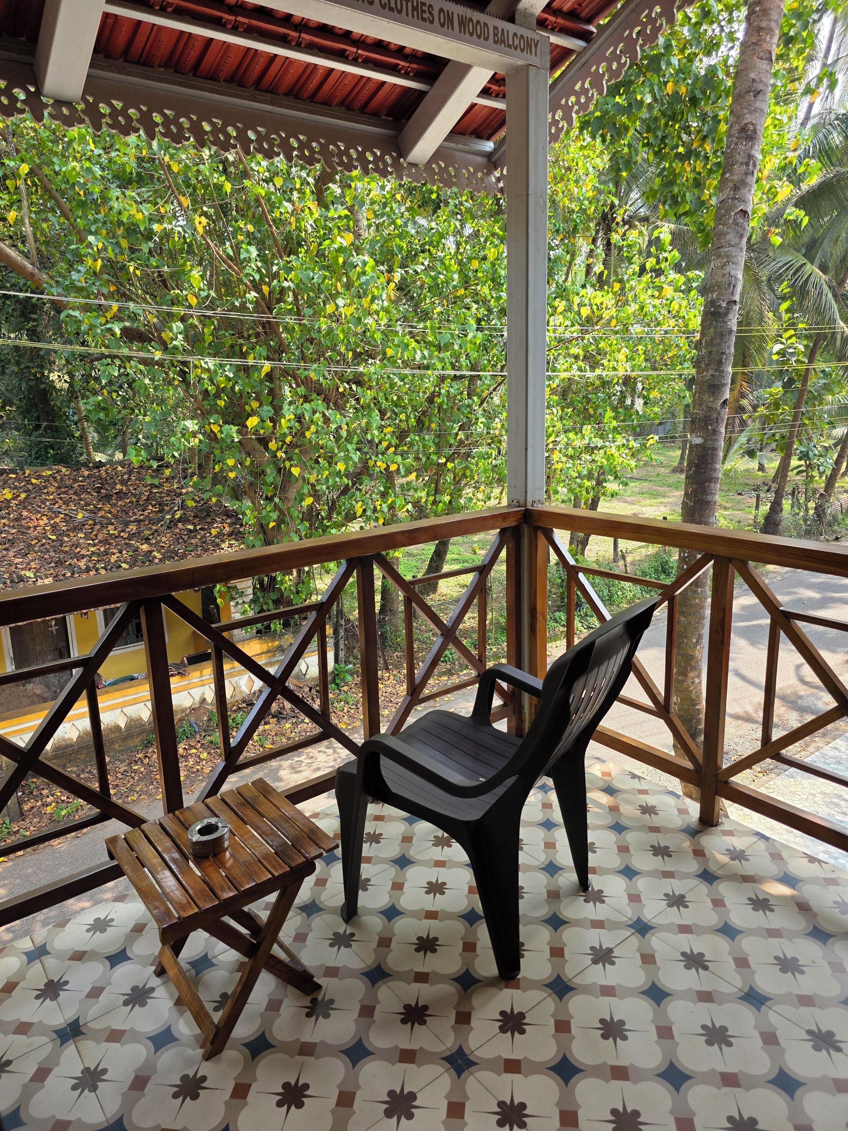 A wooden balcony with a chair and a small table, surrounded by a lattice fence and lush greenery.