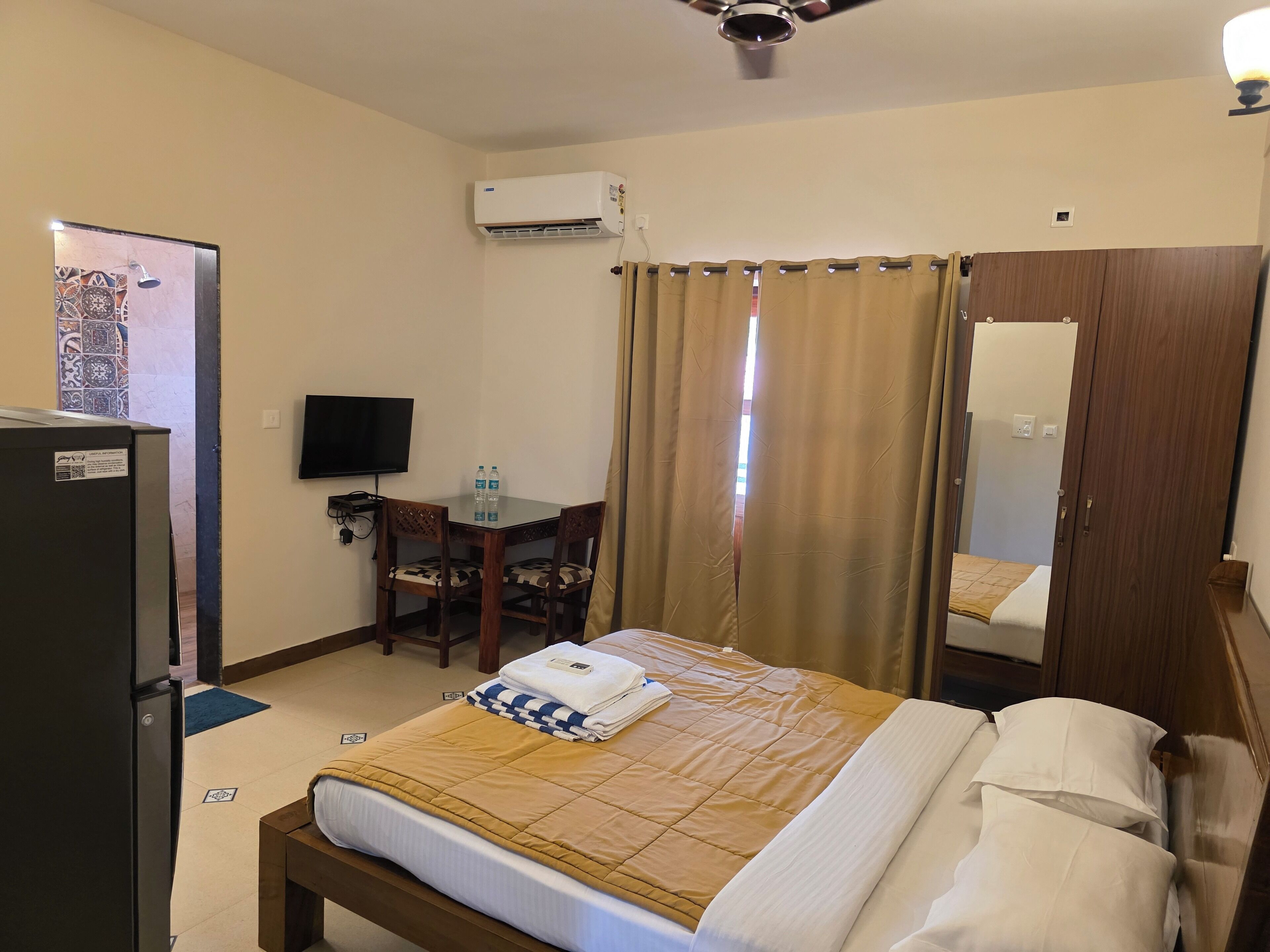 A hotel room with a bed, a desk with a chair, a television, an air conditioning unit, and a wardrobe.