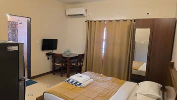 A hotel room with a bed, a desk with a chair, a television, an air conditioning unit, and a wardrobe.