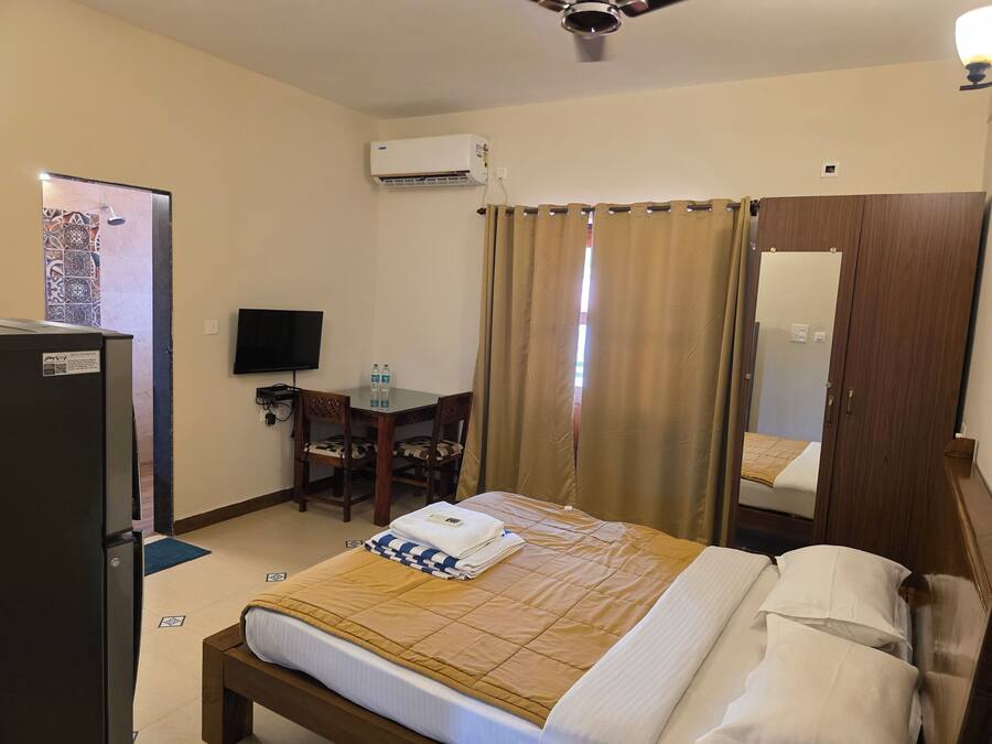 A hotel room with a bed, a desk with a chair, a television, an air conditioning unit, and a wardrobe.