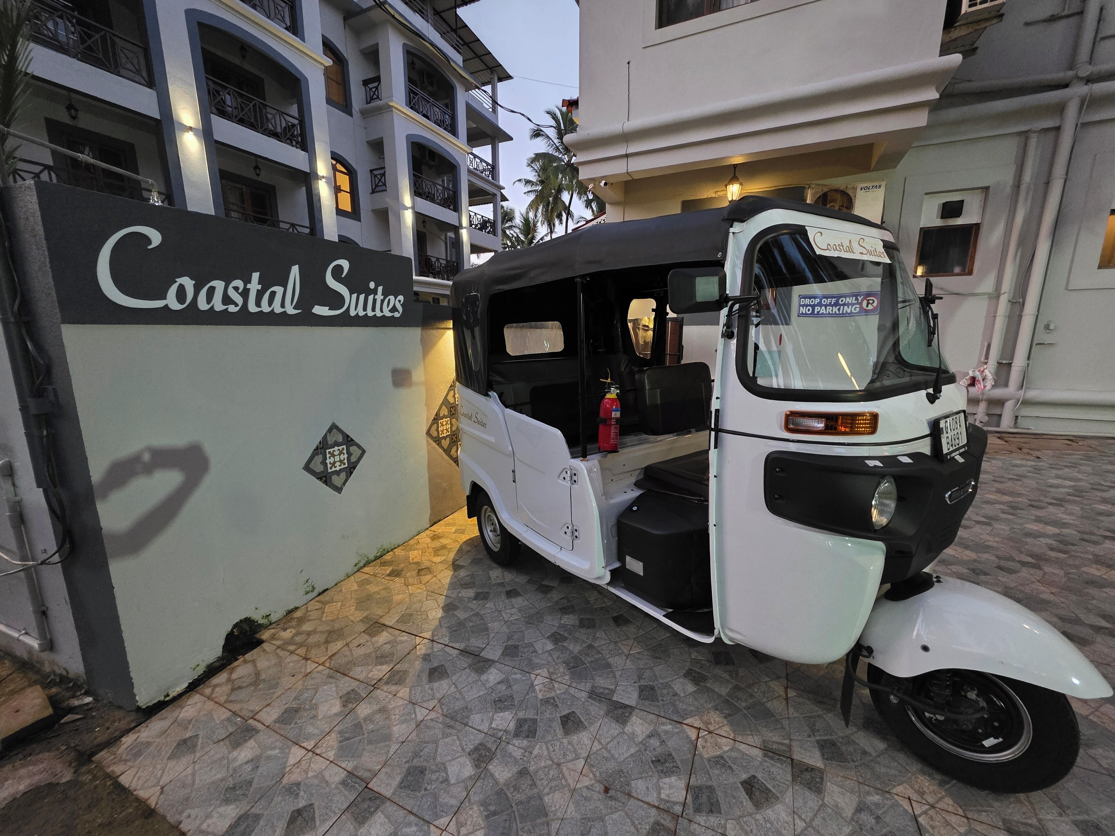 A white auto-rickshaw parked in front of a building labeled "Coastal Suites."
