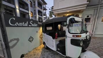 A white auto-rickshaw parked in front of a building labeled "Coastal Suites."