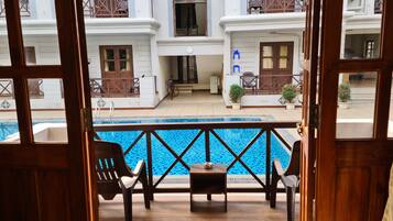 A view of a swimming pool with a wooden deck, chairs, and potted plants.