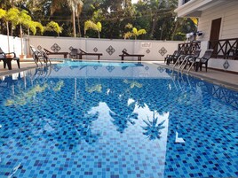 Una piscina con piso de baldosas, rodeada de sillas de descanso y una pared con un letrero.