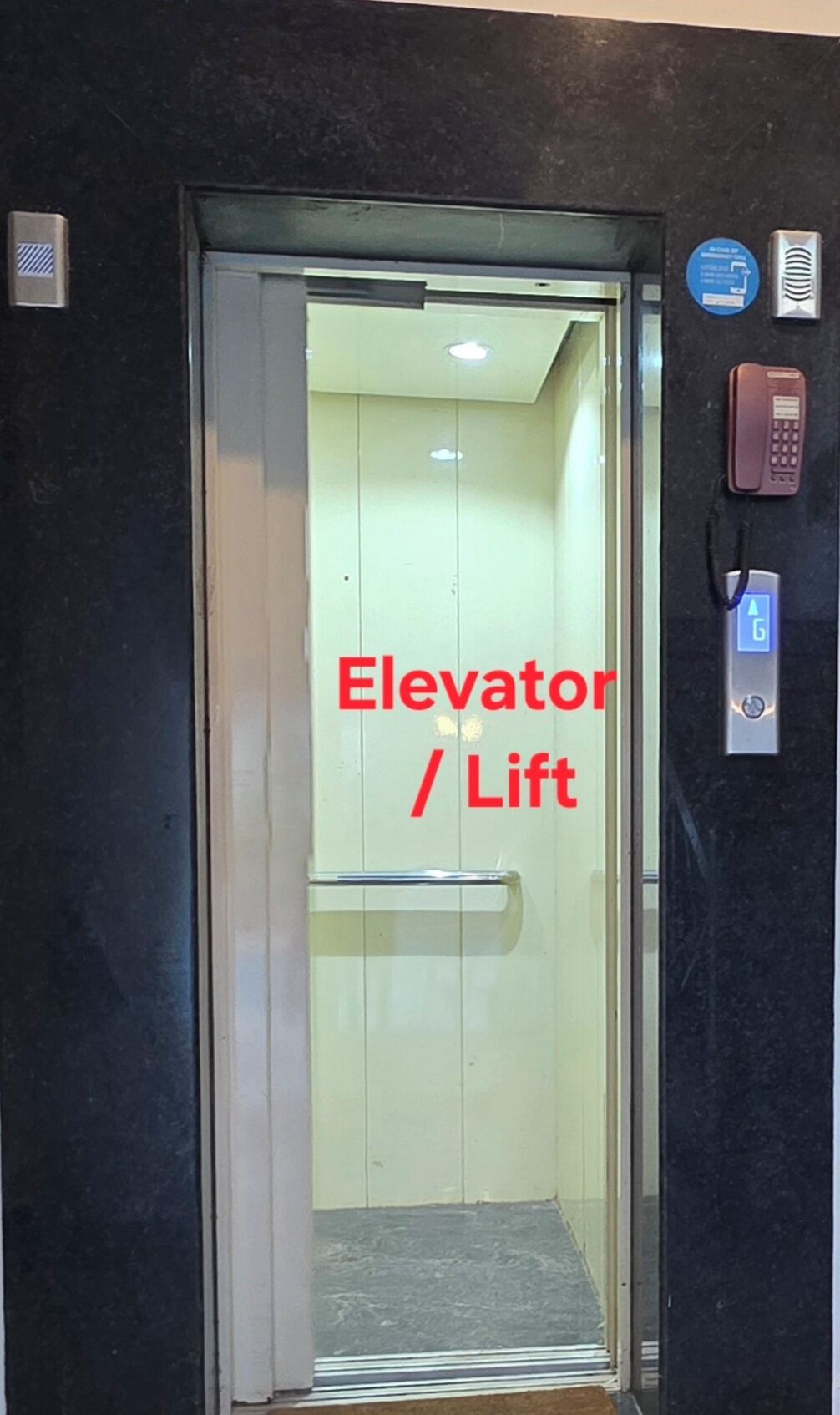 An elevator with a glass door, a red sign indicating its function, and a phone on the wall.