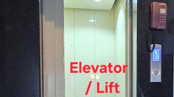 An elevator with a glass door, a red sign indicating its function, and a phone on the wall.