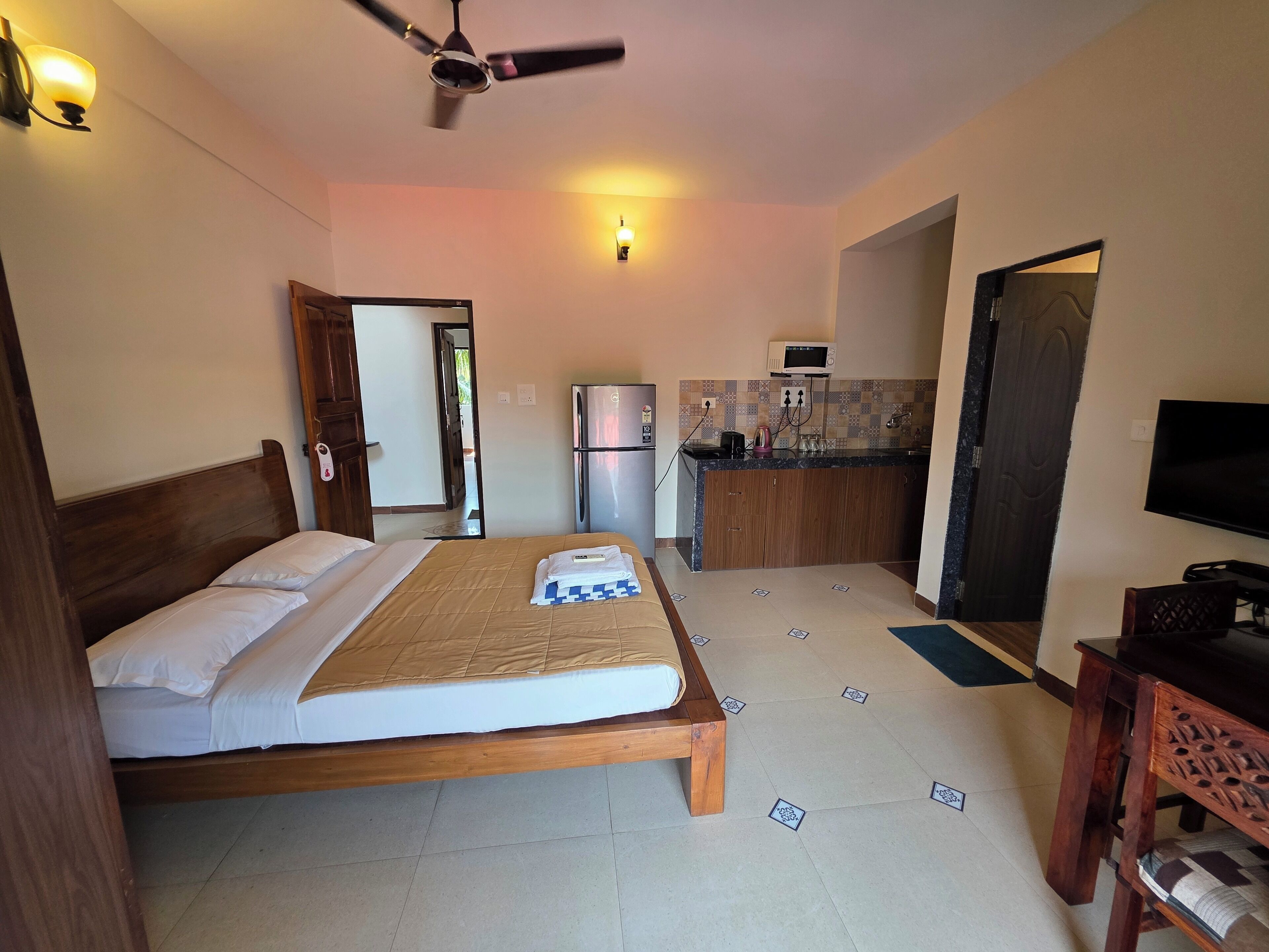 Ein Hotelzimmer mit Bett, Deckenventilator, Küchenzeile und Fernseher.