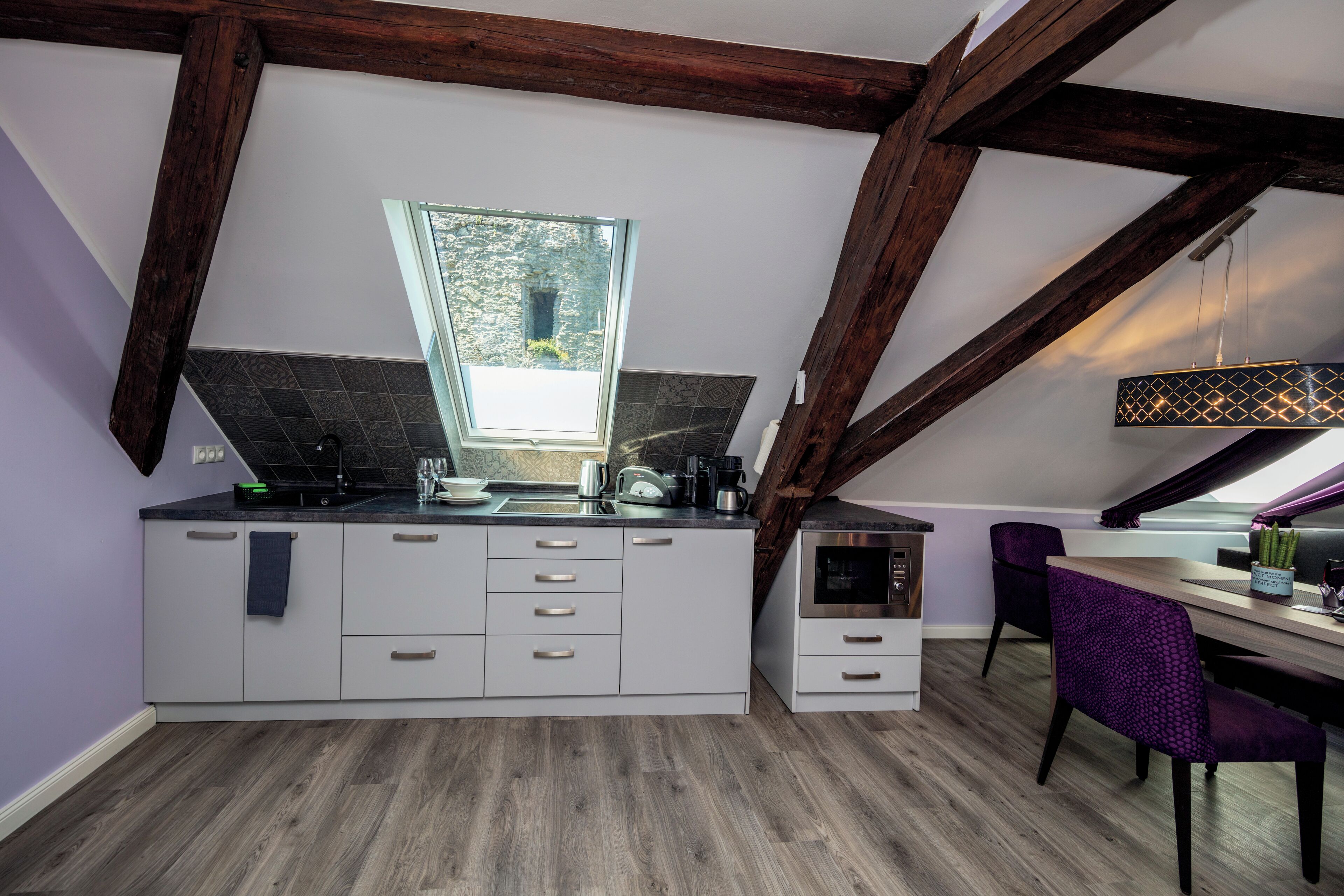 A modern kitchen with a built-in oven, a window, and a dining area with purple chairs.