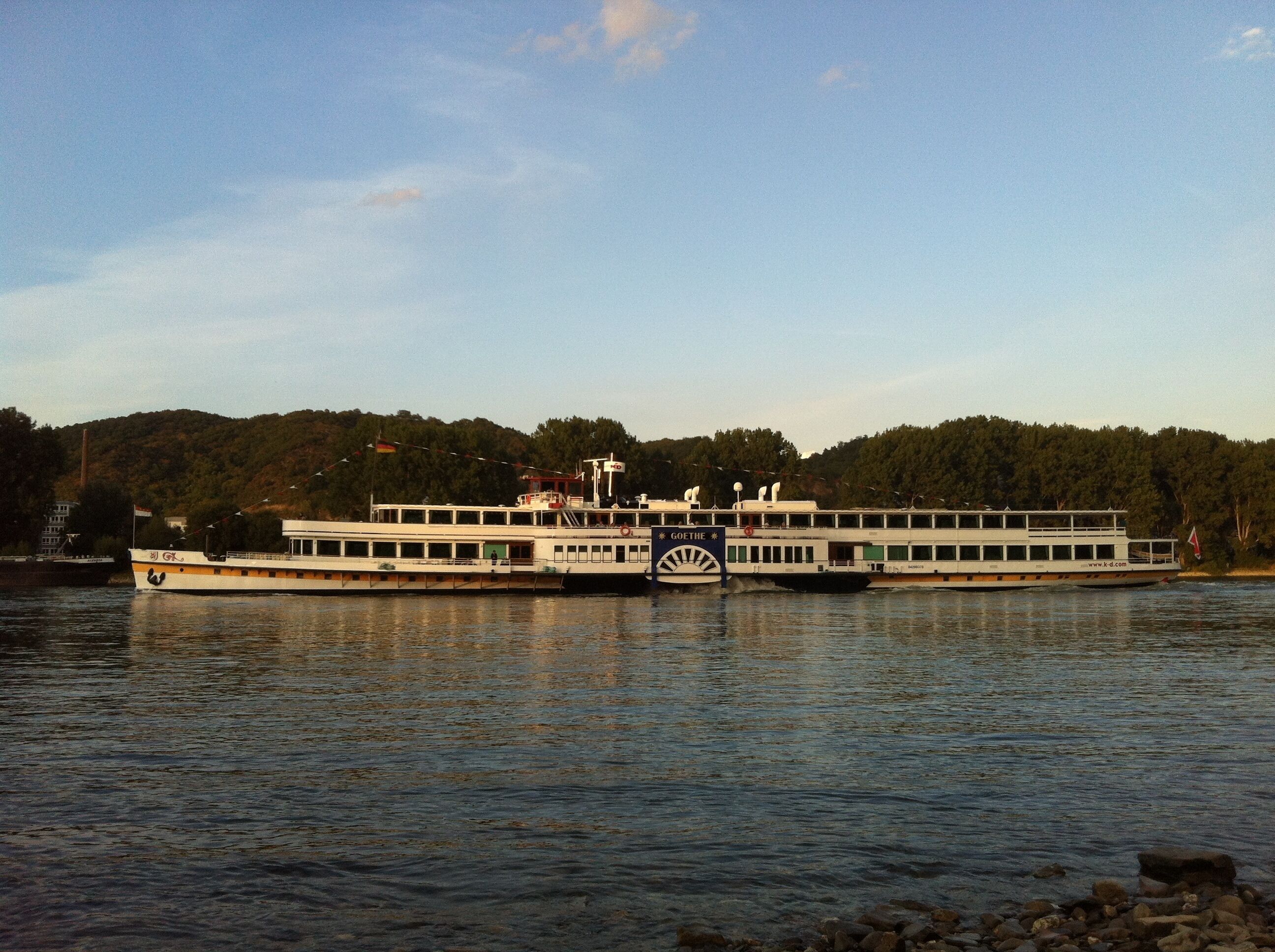 A large riverboat with multiple decks, a prominent wheelhouse, and a flag.
