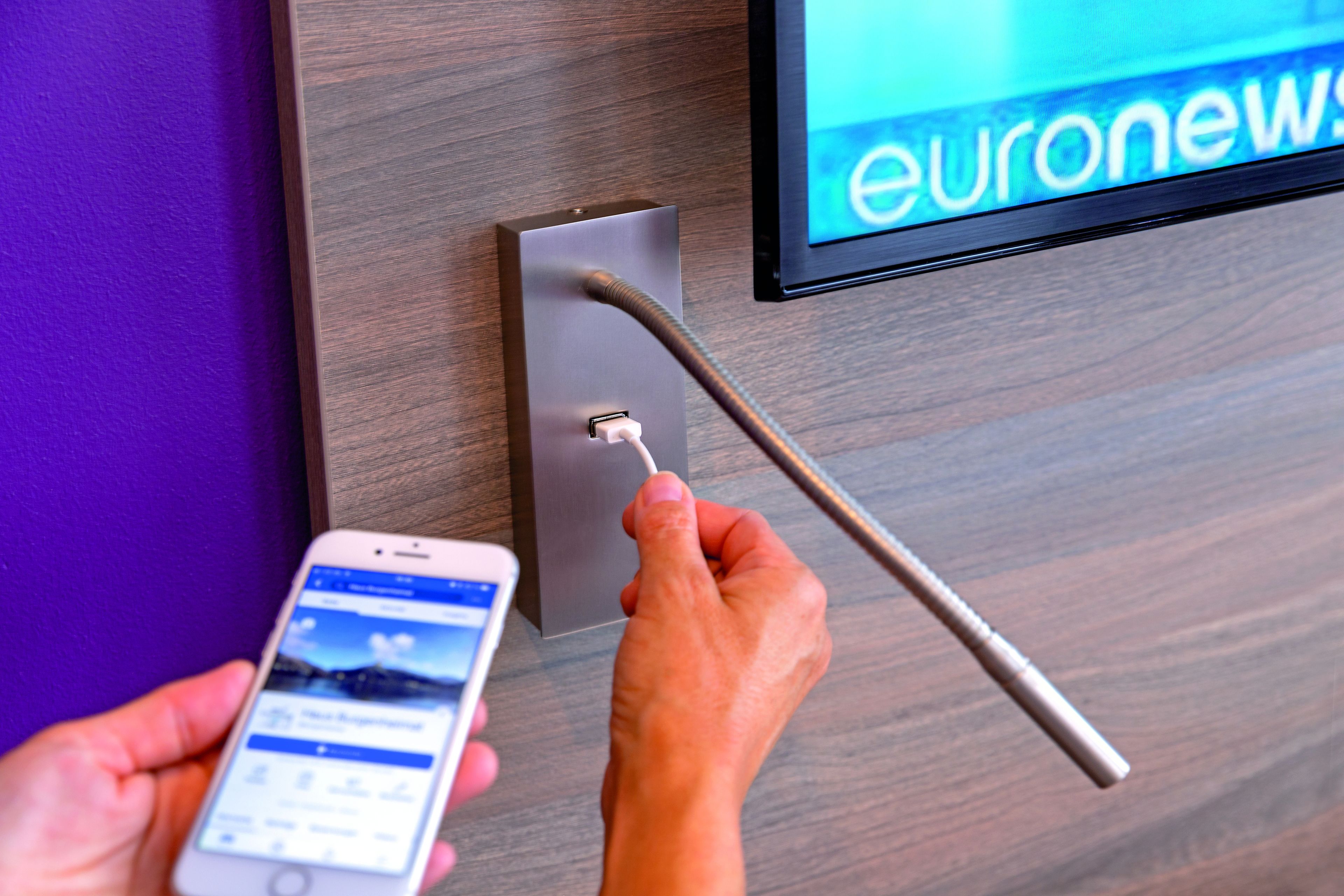 Eine Person benutzt ein Smartphone, um mit einem an der Wand montierten Gerät zu interagieren, möglicherweise für den Zugang zum Raum oder zur Steuerung.