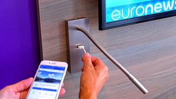 Eine Person benutzt ein Smartphone, um mit einem an der Wand montierten Gerät zu interagieren, möglicherweise für den Zugang zum Raum oder zur Steuerung.