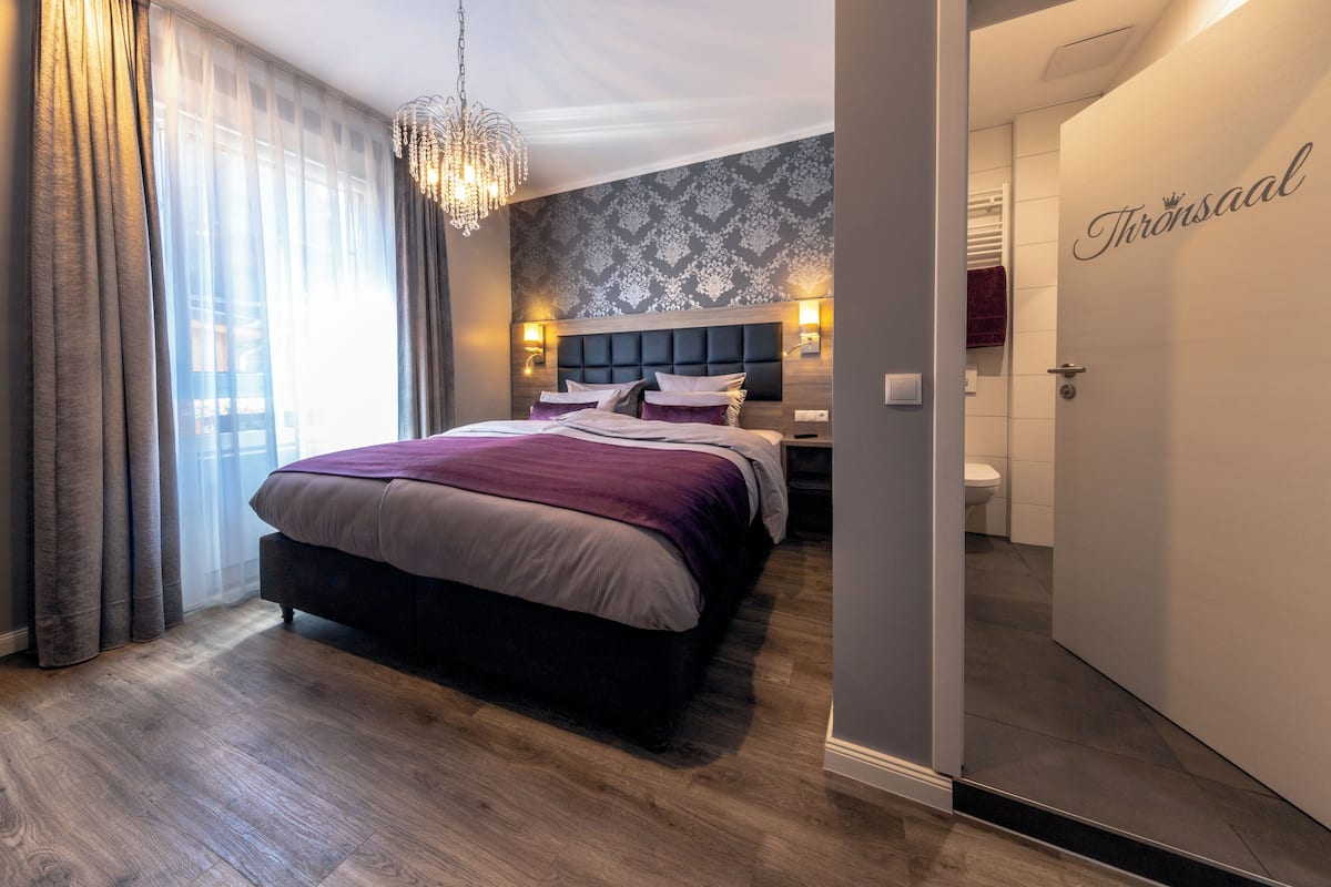 A modern bedroom with a large bed, a chandelier, and a patterned wall.