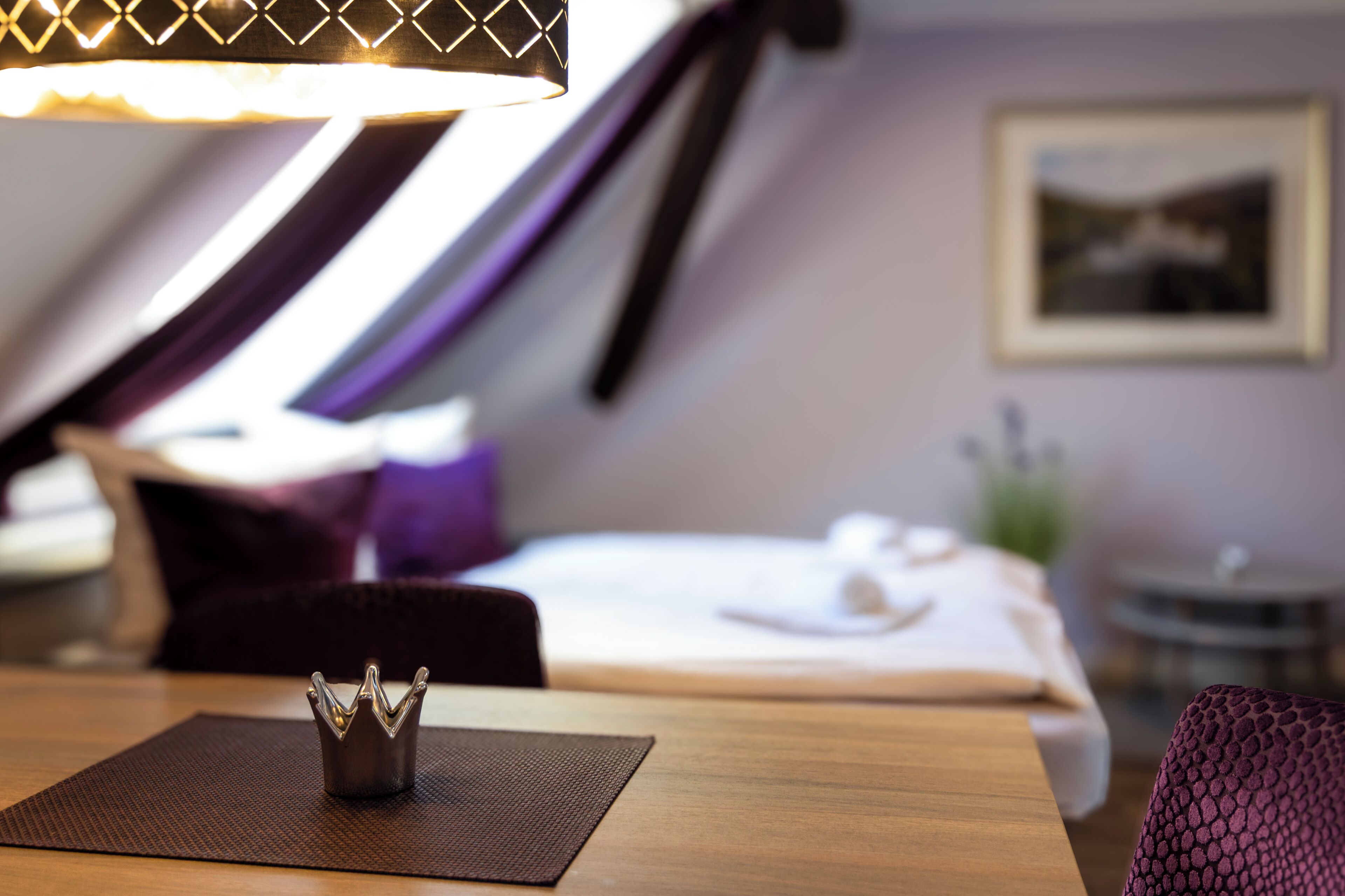 A hotel room with a bed, a small table with a decorative item, a chair, and a wall-mounted picture.