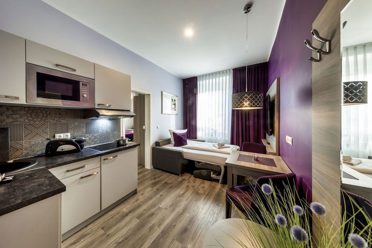 A compact hotel room with a kitchenette, a dining area, and a living space.