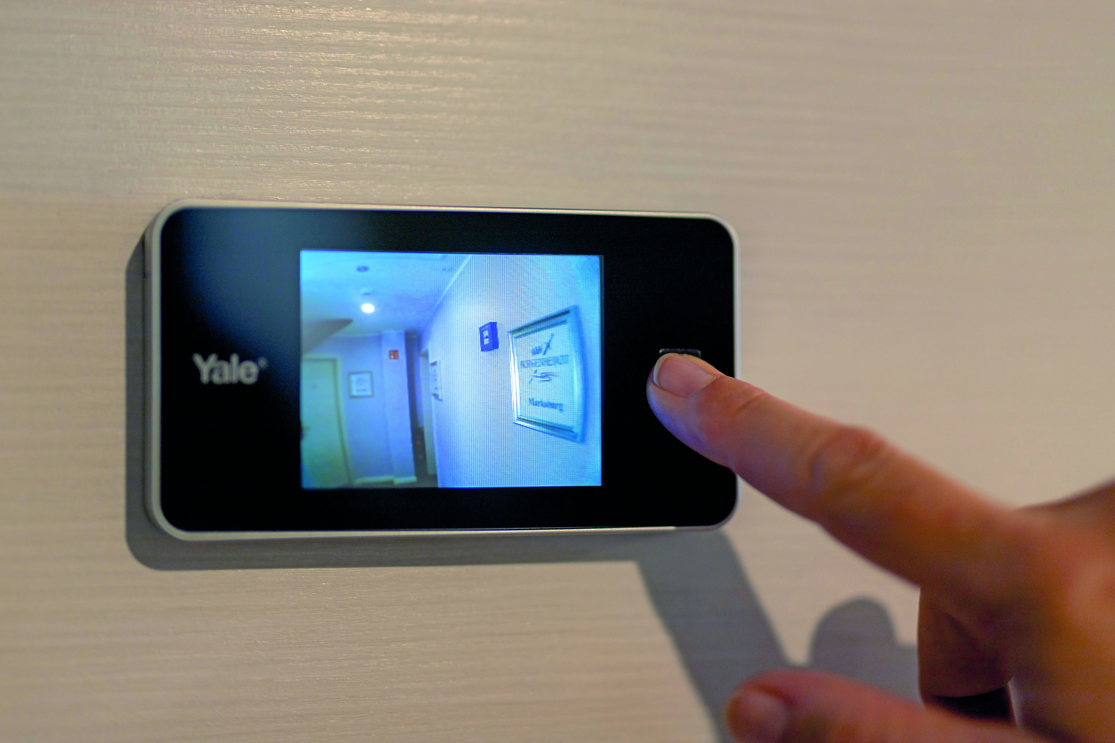 Une serrure intelligente de la marque Yale est installée sur une porte, donnant sur un couloir avec d’autres portes et une signalétique.