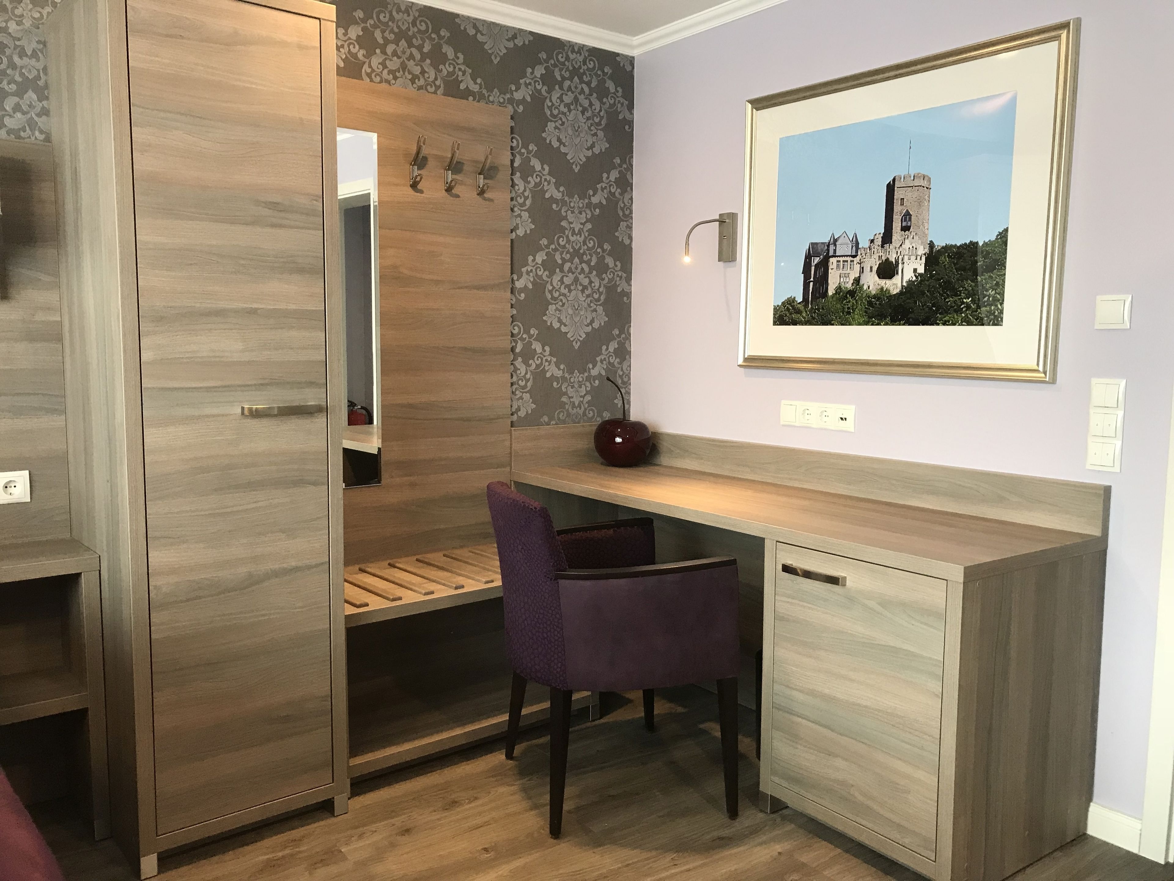 A modern room with a wooden desk, a purple chair, a framed picture on the wall, and a wardrobe with a mirror.