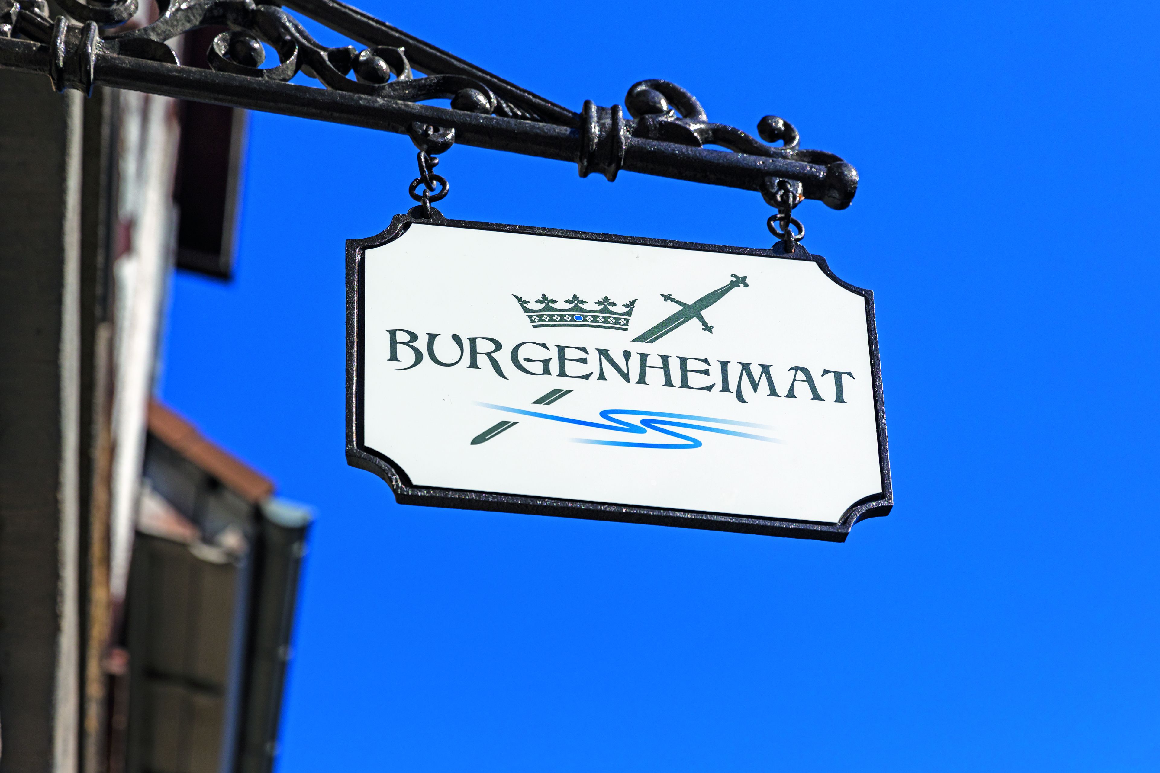 En skylt med texten ”BURGENHEIMAT” och en symbol bestående av en krona och ett svärd.