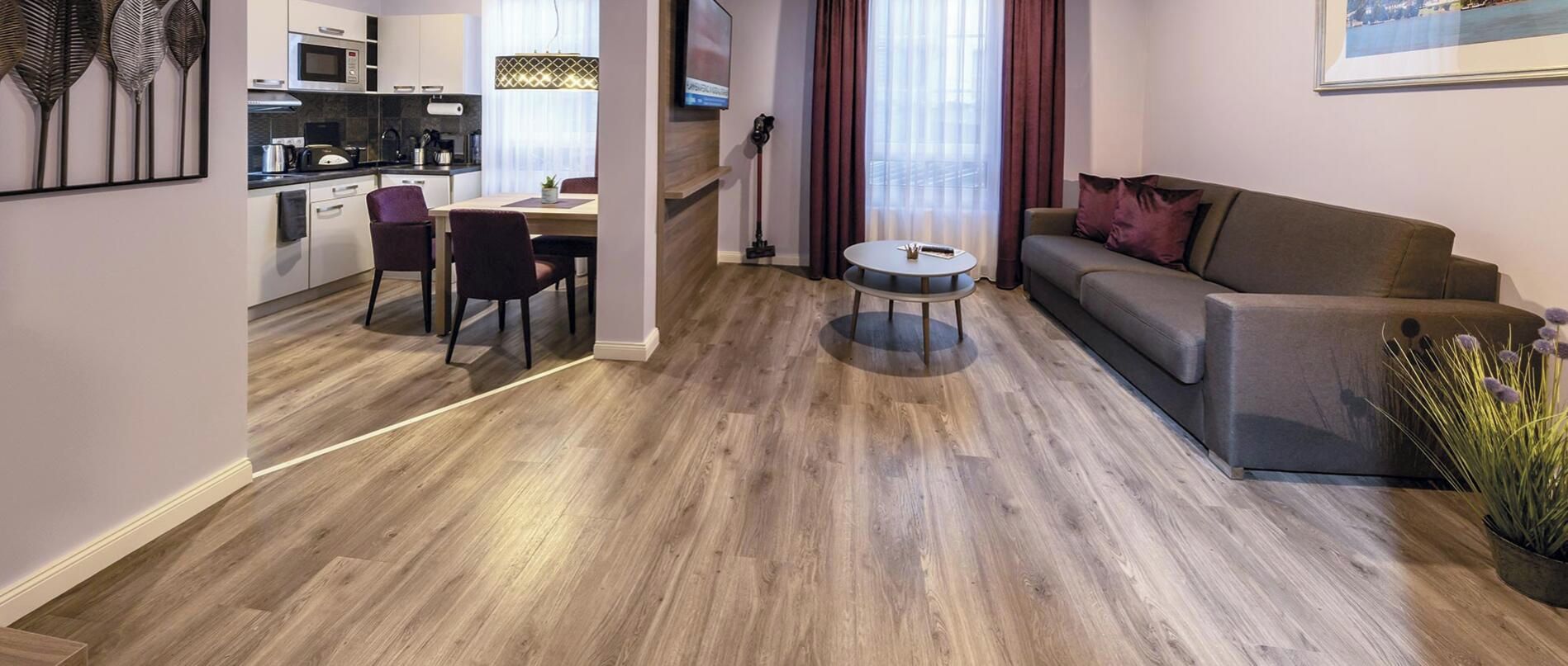 Ein modernes Wohnzimmer mit einer Couch, einem Esstisch mit Stühlen und einer Küchenzeile mit Schränken und Geräten.