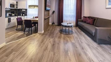 Ein modernes Wohnzimmer mit einer Couch, einem Esstisch mit Stühlen und einer Küchenzeile mit Schränken und Geräten.