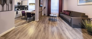 A modern living room with a sofa, a dining table with chairs, and a kitchen area with cabinets and appliances. - Burgenheimat (Rhens)