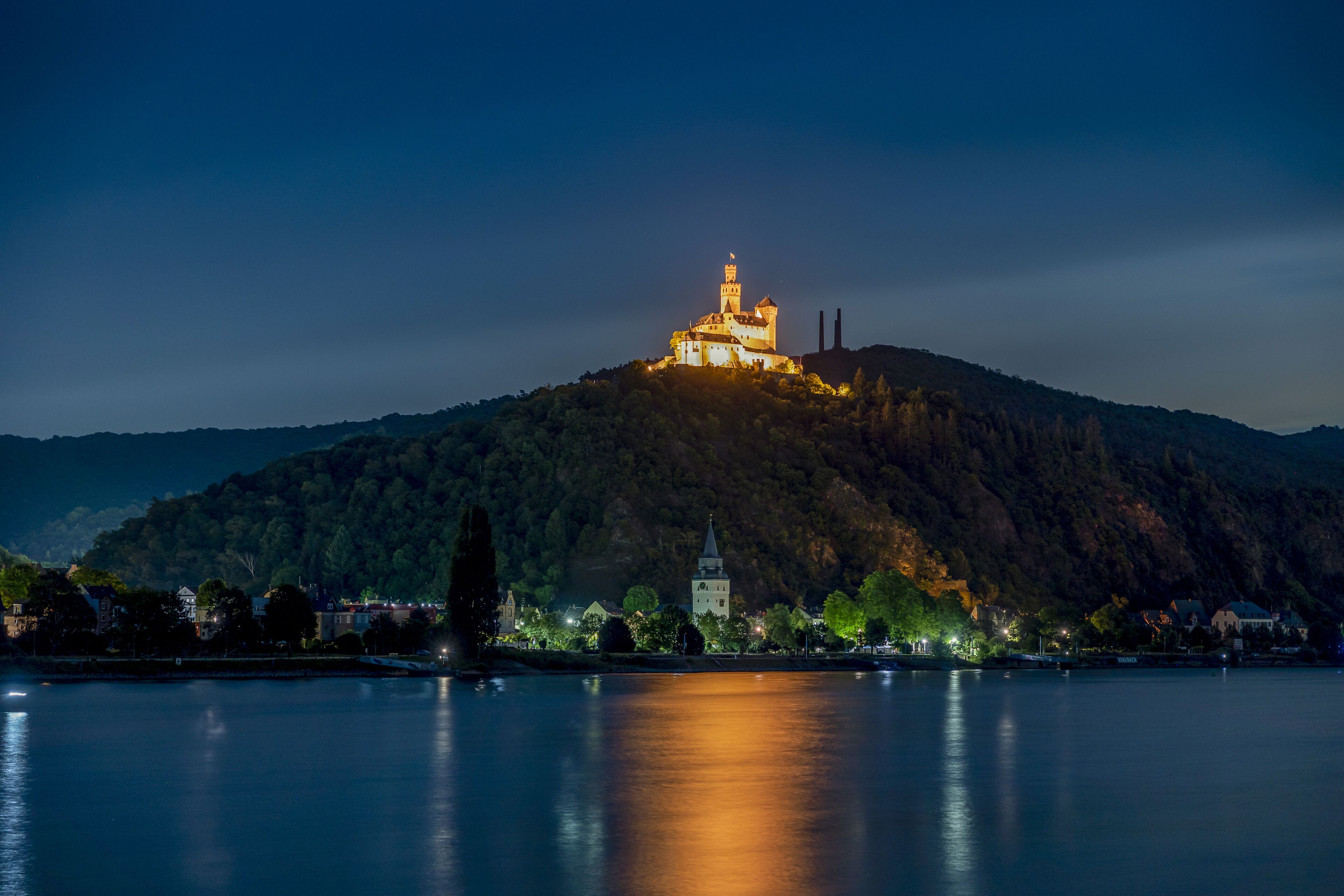 Een kasteel op een heuvel met uitzicht op een kalm meer in de nacht.