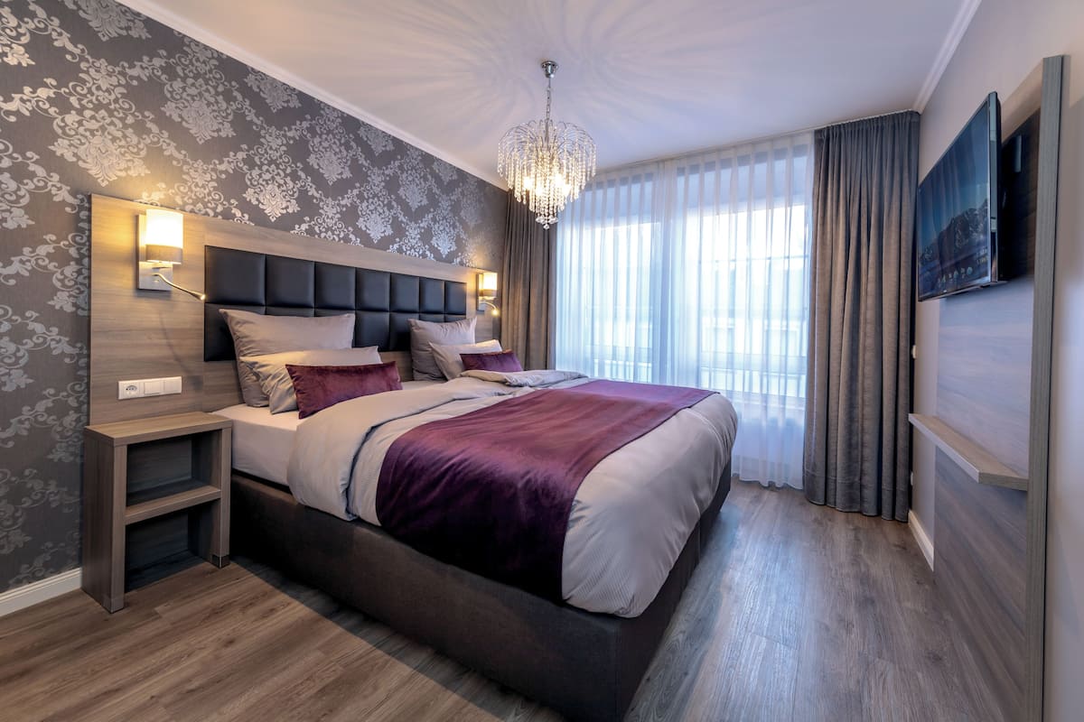 A modern hotel room with a large bed, a nightstand, a wall-mounted TV, and a chandelier.