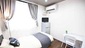 Una habitación pequeña con cama, escritorio y aire acondicionado.