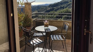 An open patio with a round table and chairs, a glass of drink, and a view of a hilly landscape. - Elegant Holiday Home, in the Village (Badolato)