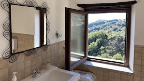A bathroom with a large mirror, a sink, and a window offering a view of a forested hillside. - Elegant Holiday Home, in the Village (Badolato)