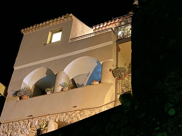 Un bâtiment doté d’un toit en pente, d’un balcon orné de plantes en pot et d’une fenêtre.