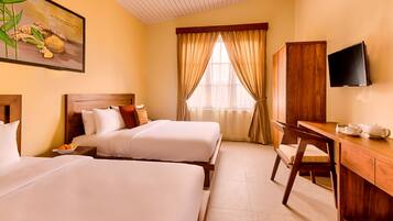 A hotel room with two beds, a wooden desk, a television, and a window with curtains.