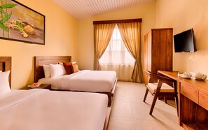 Habitación de hotel con dos camas, un escritorio de madera, televisión y una ventana con cortinas.