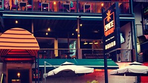 A restaurant with outdoor seating, a sign advertising happy hour, and a neon sign for a club. - Spice Ella (Ella)
