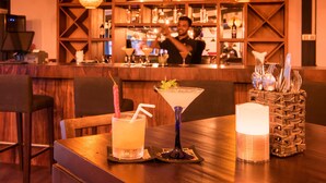 A bar area with wooden decor, a bartender, and two drinks on a table. - Spice Ella (Ella)