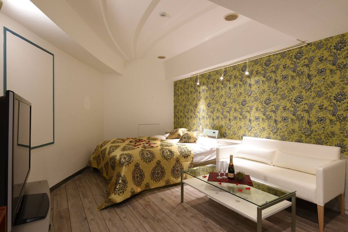 A bedroom with a bed, a white sofa, a glass coffee table, and a wall with floral wallpaper.