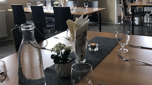 Un coin repas avec des tables préparées pour deux personnes, comprenant de la vaisselle transparente, une bouteille et une bougie.